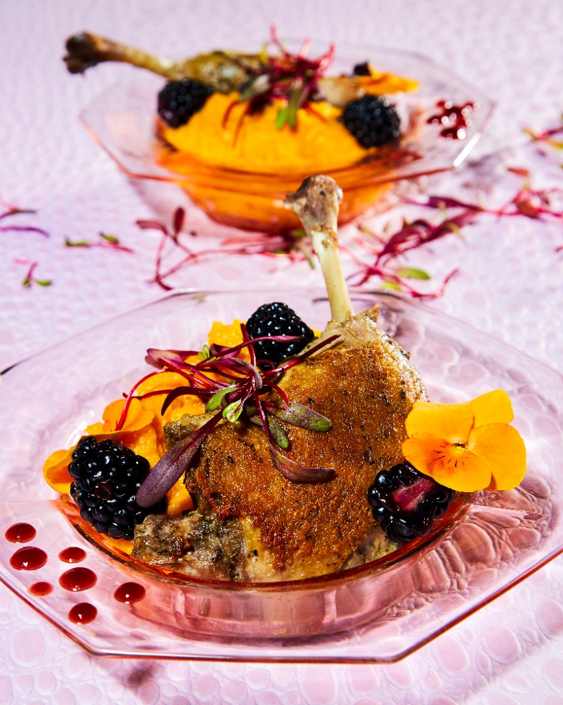 Duck confit with blackberry garnish on a pink plate